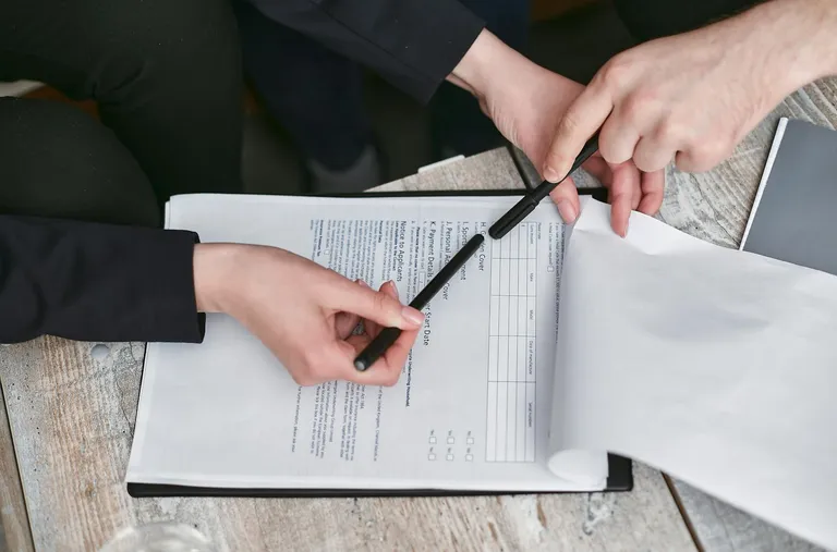 Close-up of business hands reviewing and signing a contract document with a pen
