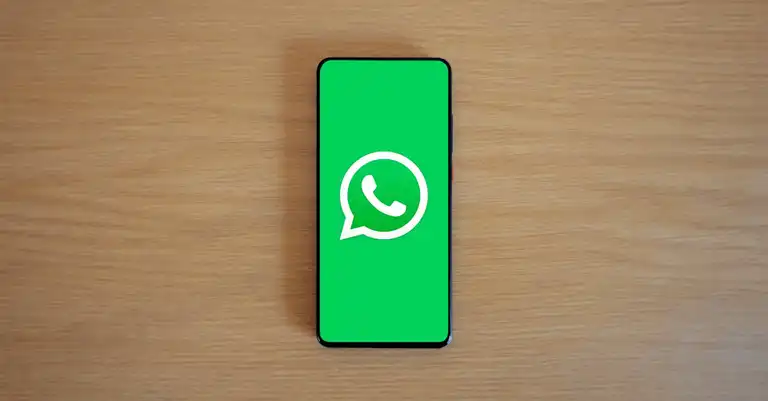 Smartphone displaying WhatsApp logo on a wooden surface